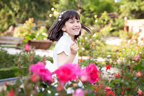 Niña bailando entre flores, en la Rosaleda del Parque del Oeste. Lleva un vestido blanco y una corona en la cabeza, está en una sesión de fotos de primera comunión en Madrid.